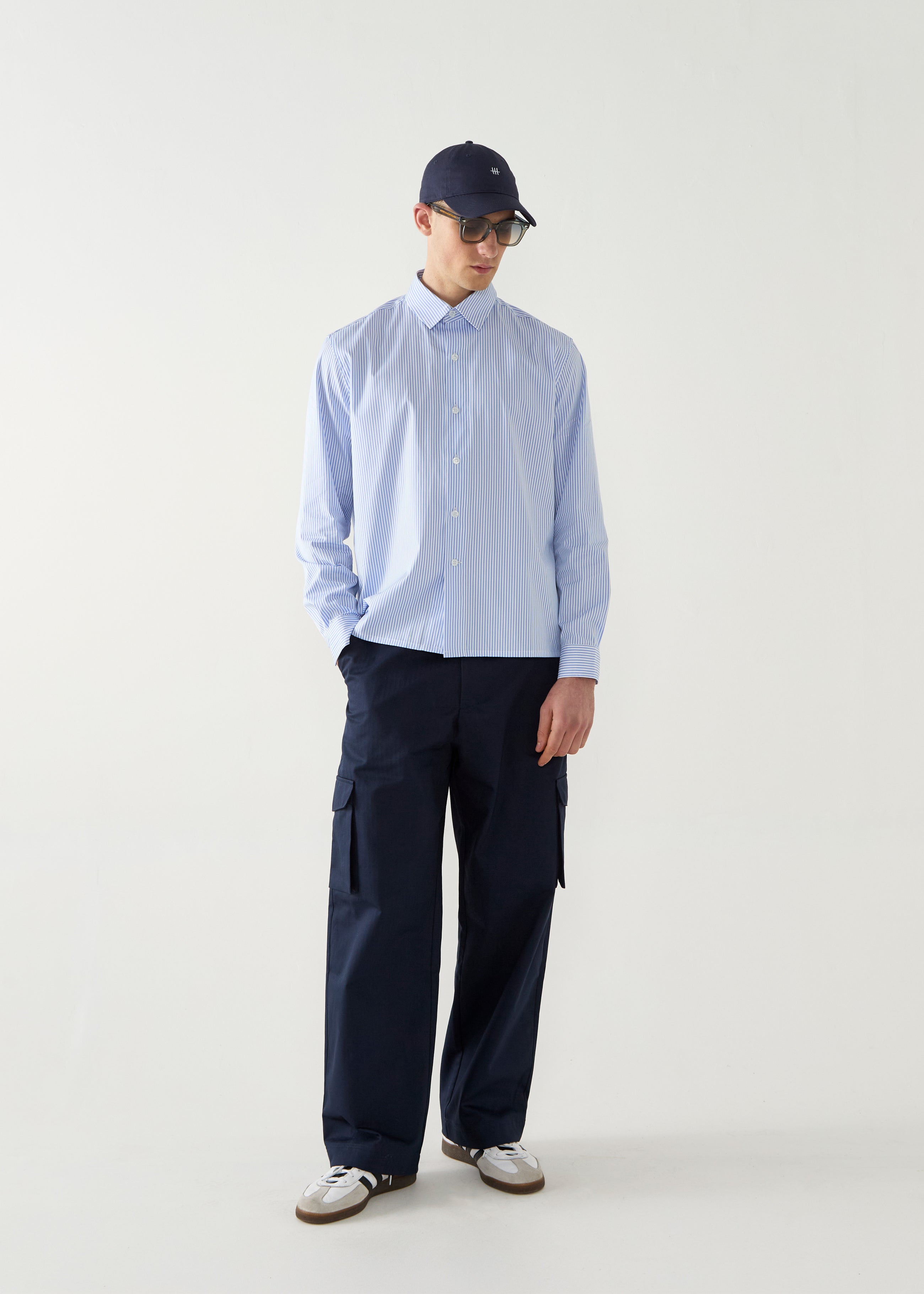 Person wearing a light blue striped shirt and navy pants with a cap on a white background