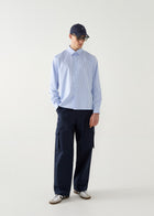Person wearing a light blue striped shirt and navy pants with a cap on a white background
