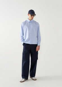 Person wearing a light blue striped shirt and navy pants with a cap on a white background